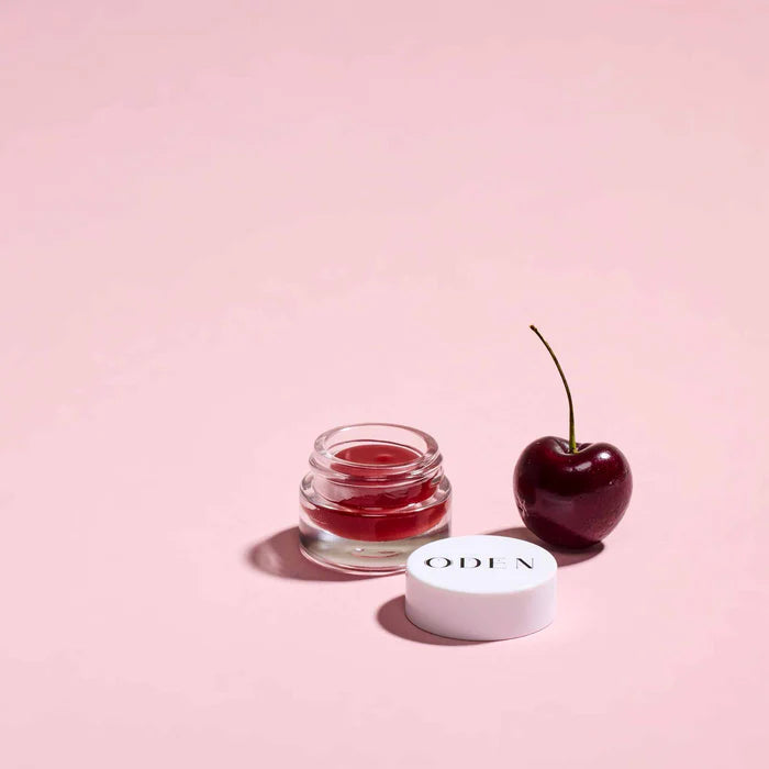 ODEN French Lip Balm Cherry geöffnet mit Balm und Kirsche auf rosafarbenem Hintergrund