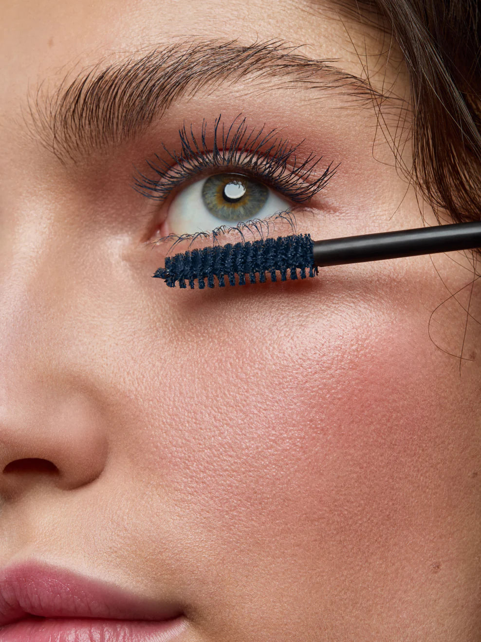 Nahaufnahme eines Auges beim Auftragen der blauen Mascara